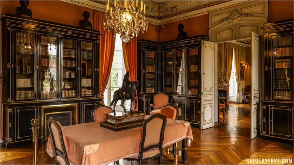 Bibliothèque du château : vitrines de bois noirci garnies d'ouvrages reliés, bronze équestre et lustre.