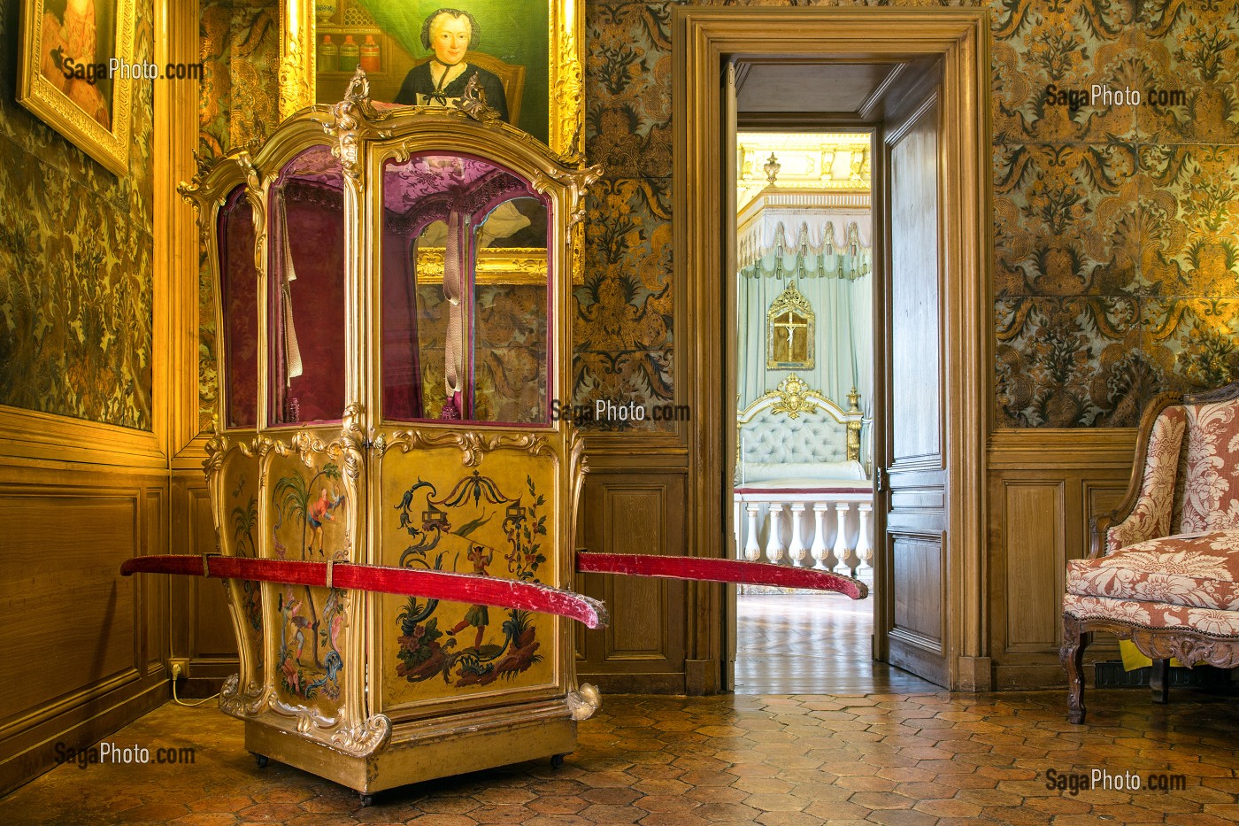 Un appartement du château : chaise à porteurs dorée à décor de chinoiseries, boiseries de chêne, et la chambre à l'alcôve aperçue par la porte ouverte.