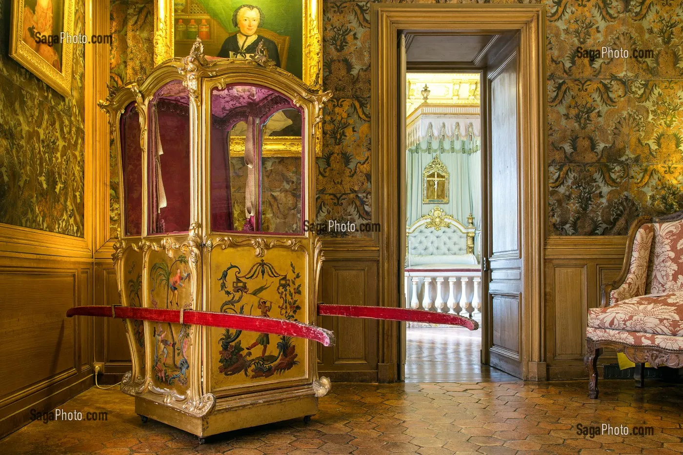Un appartement du château : chaise à porteurs dorée à décor de chinoiseries, boiseries de chêne, et la chambre à l'alcôve aperçue par la porte ouverte.